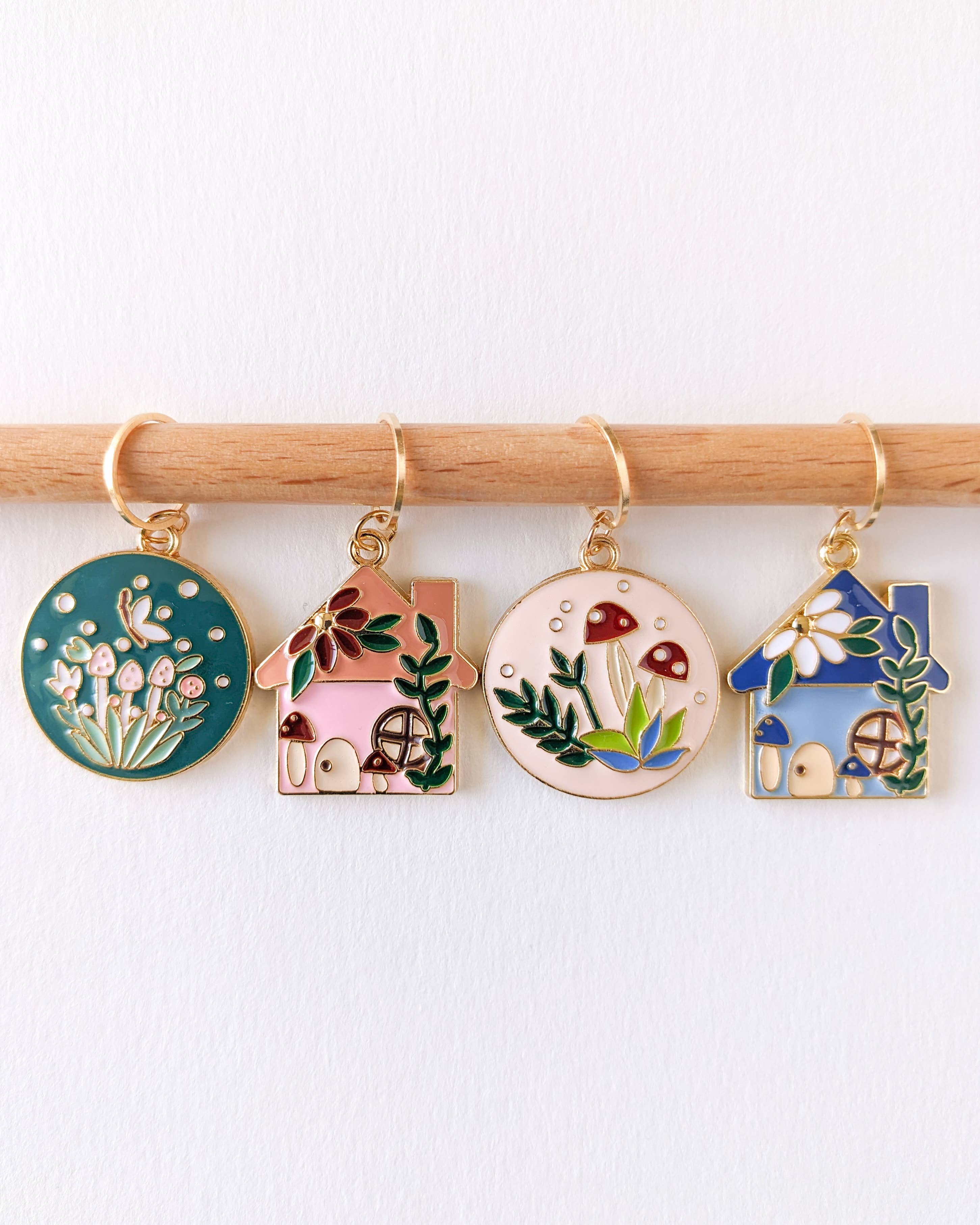 Set of four colorful enamel fairytale house and forest ring stitch markers on a knitting needle against a white background