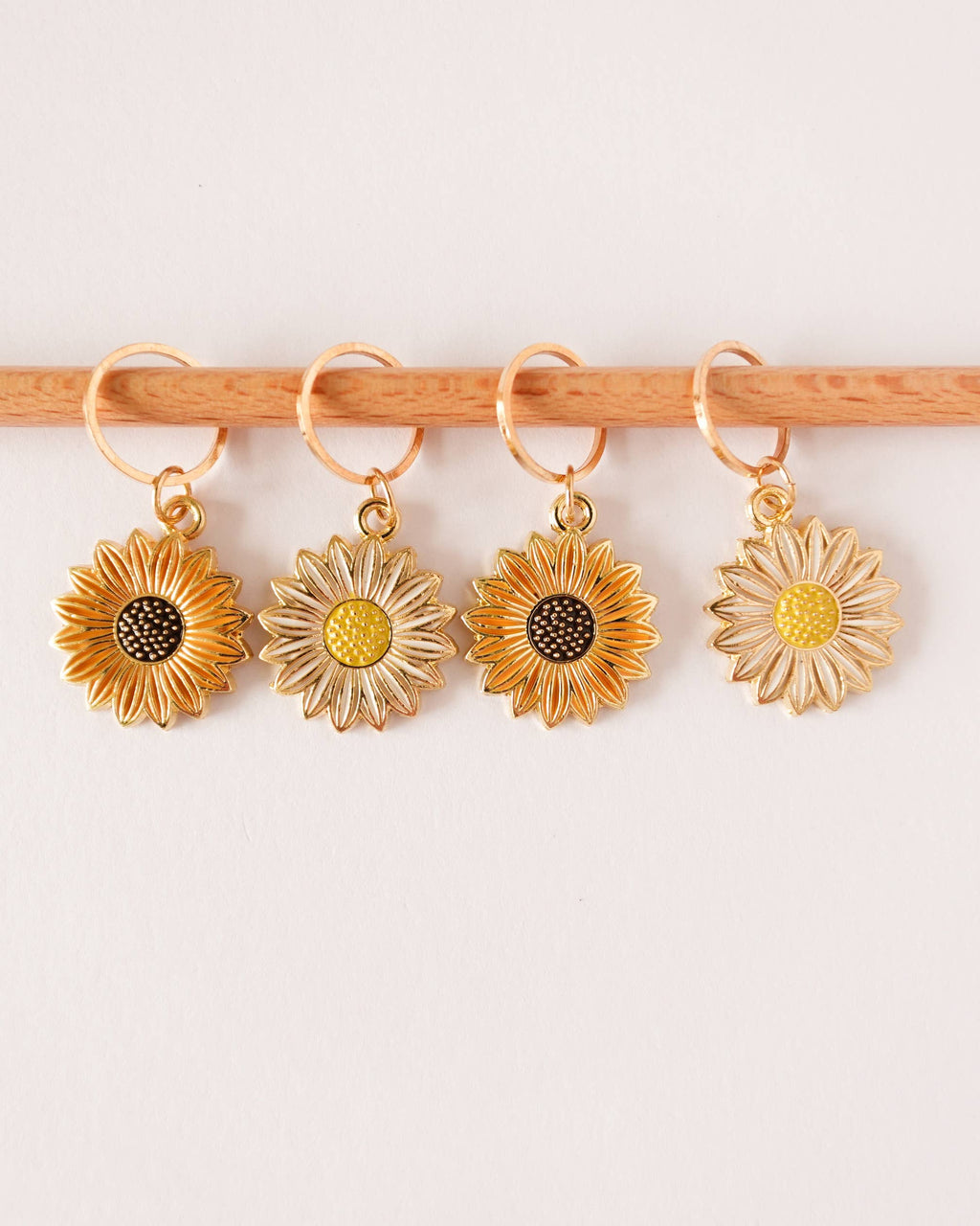 Four gold, white and orange sunflower-shaped stitch markers on a knitting needle against a white background