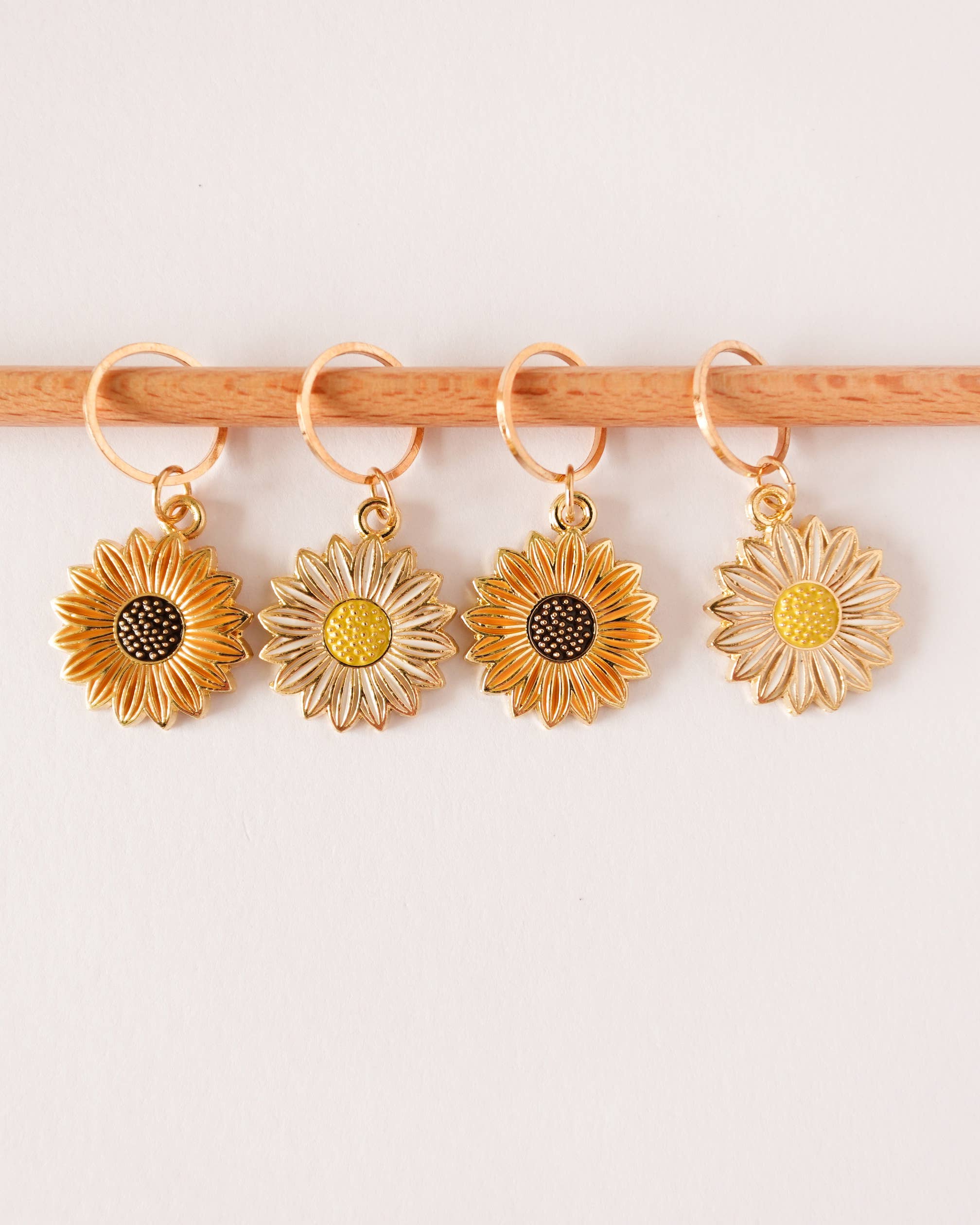 Four gold, white and orange sunflower-shaped stitch markers on a knitting needle against a white background