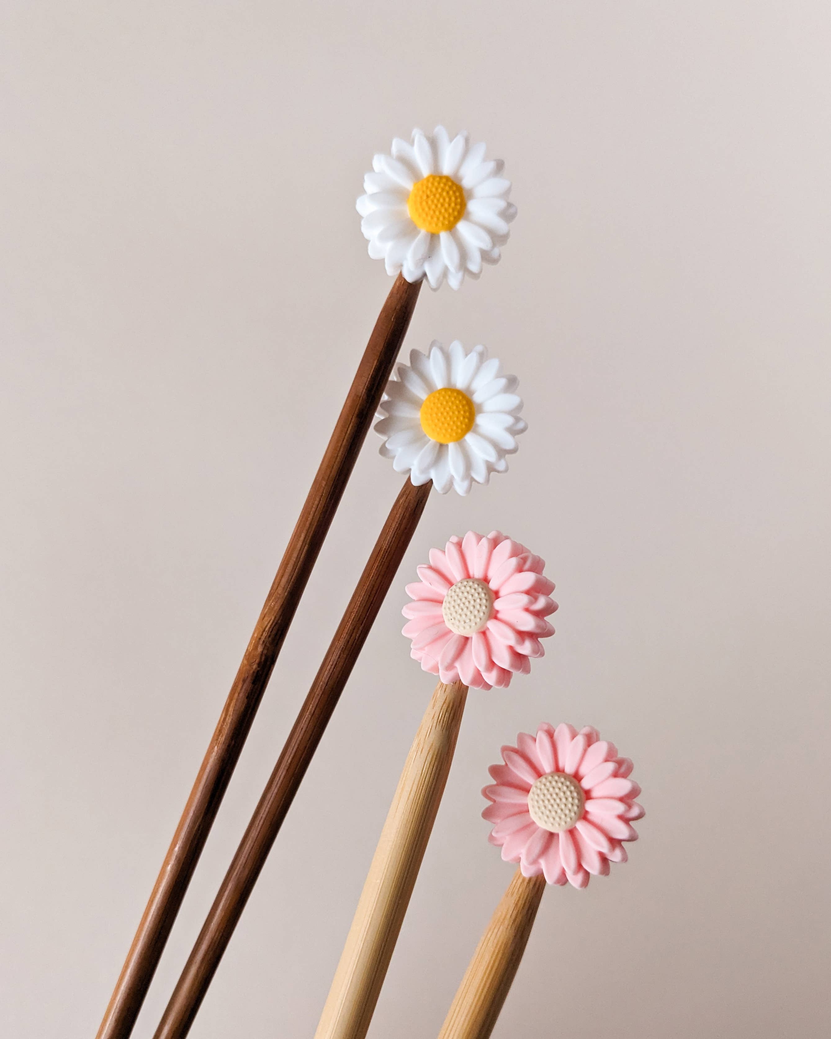 Four stitch stoppers for knitting needles in the shape of pink and white daisies