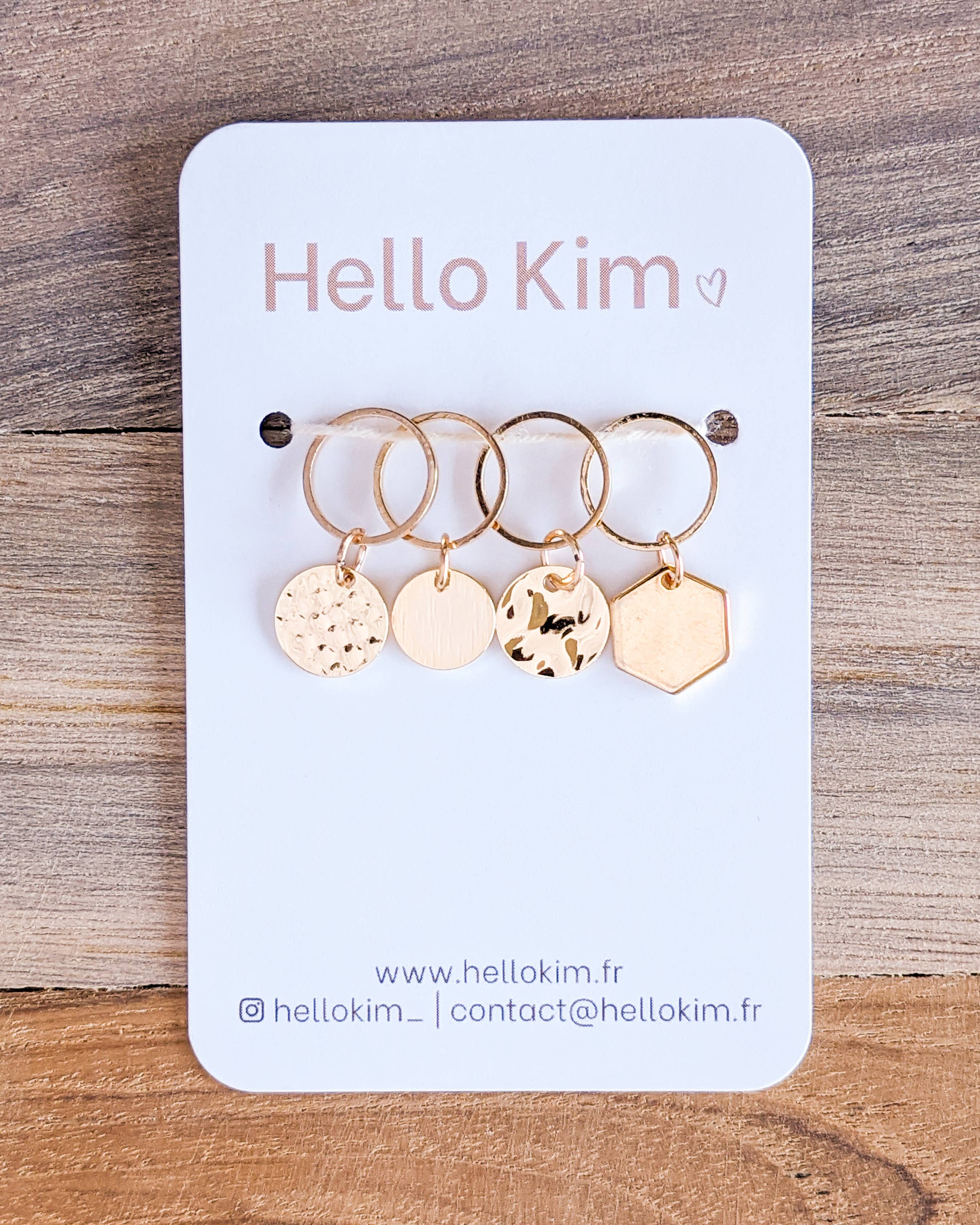 Set of four gold stitch markers on a 'Hello Kim' branded card with a wooden background